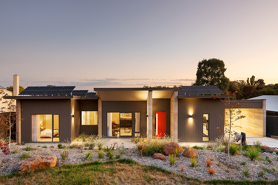 North facade of a sustainable rammed earth and light-weight clad home at dusk
